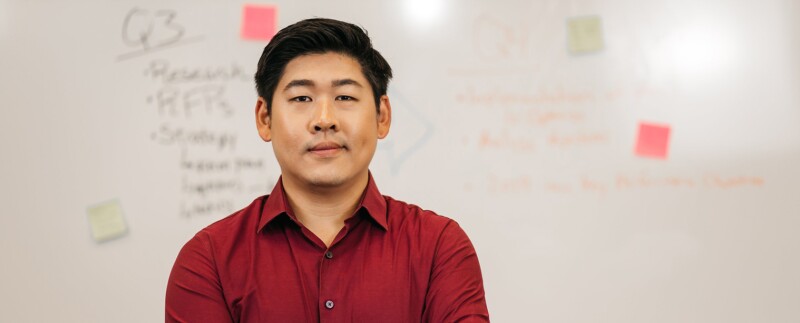 Asian man standing in front of a whiteboard with writing and sticky notes.