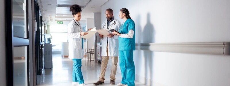 Three healthcare professionals standing in the hallway of a hospital going over charts
