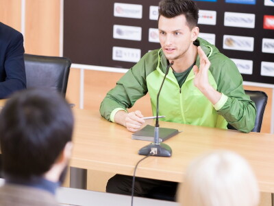 An athlete and a manager sit in the press room after a game speaking to the press.