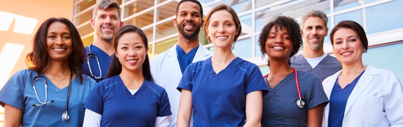 Smiling team of diverse nursing professionals standing together outside a hospital.