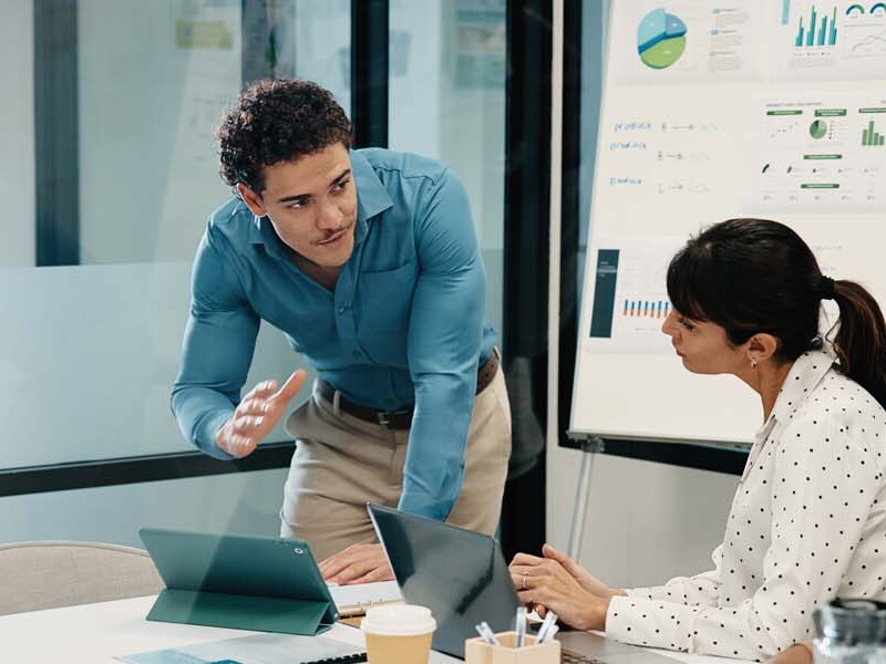 A business team meeting around a table in a modern office near a whiteboard and laptops.