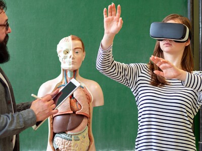 Young teacher using Virtual Reality Glasses and 3D presentation to teach students in biology class.