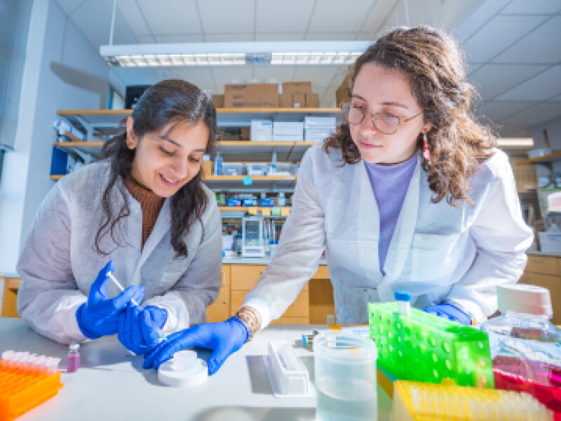 Close-up of two female CWRU biomedical engineering students using a syringe to draw a sample.