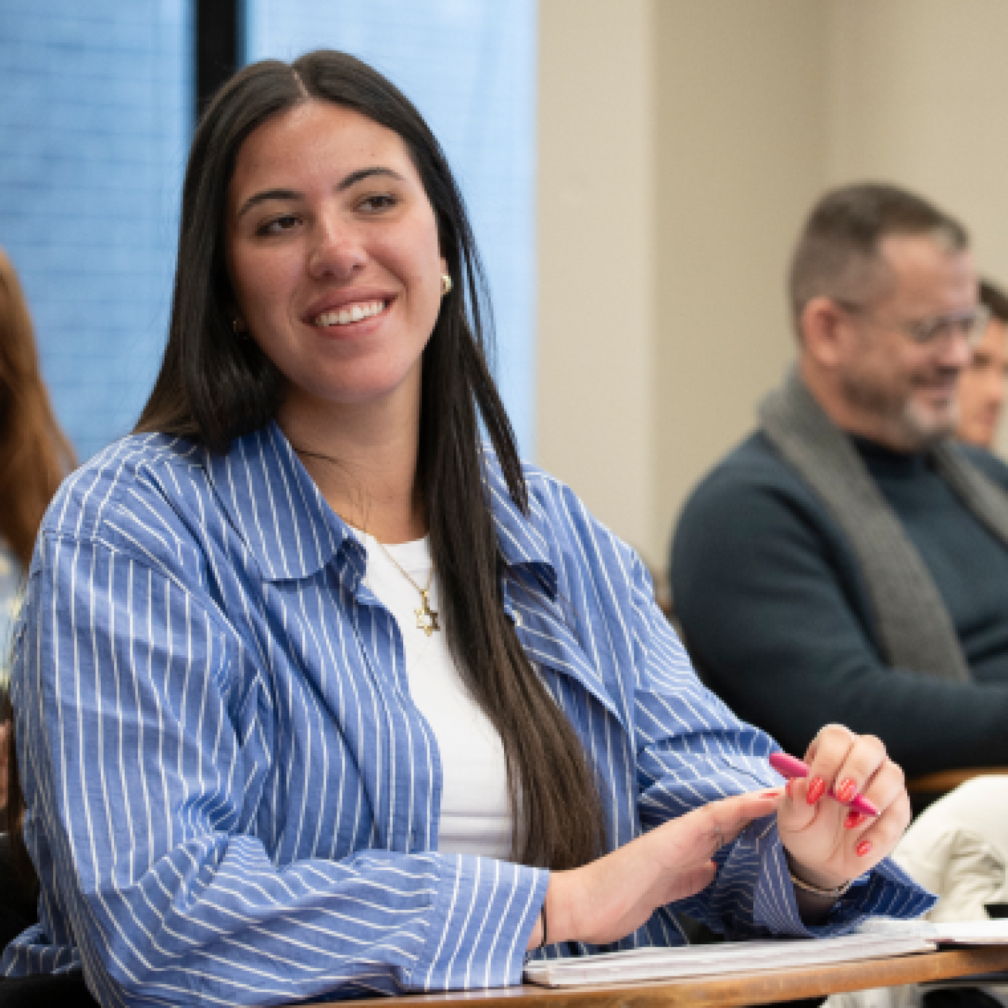 A young female student smiles while listening to a professor's lecture in the classroom.