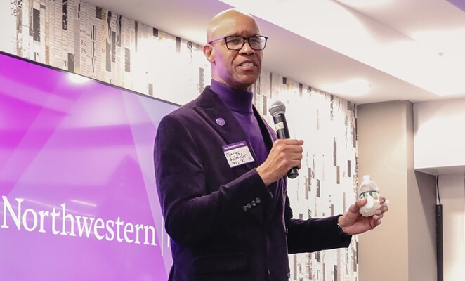 Man in blazer speaking in front of Northwestern sign
