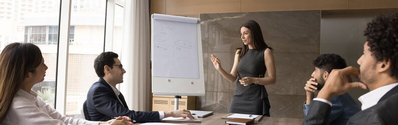 A diverse business team and a female project leader discussing work strategy at a meeting table.