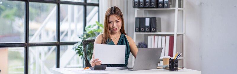 A woman sitting at a desk, reading a piece of paper.