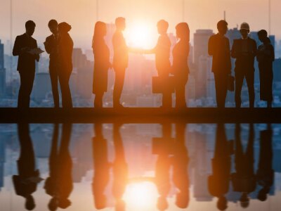 Silhouettes of business professionals standing in a high-rise corporate office as the sun rises.