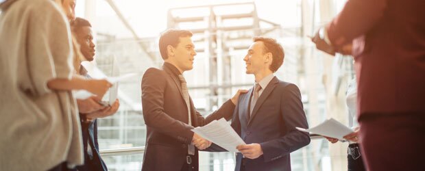 Two men in suits shake hands as they discuss ethics in corporate governance.
