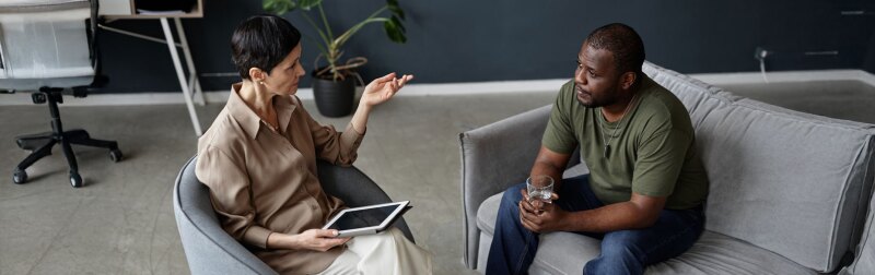 female psychologist in sitting therapy session with army veteran holding a glass of water.