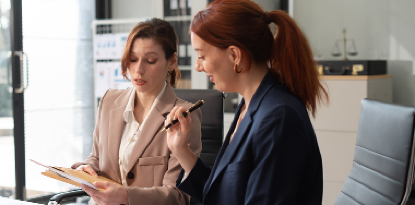 two women at a desk conversing over paperwork