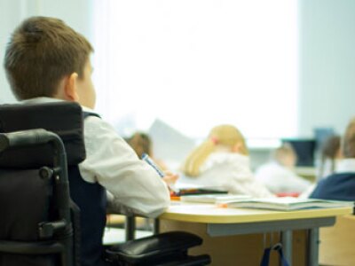 Student in a wheelchair sits at a desk in a classroom.