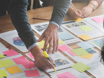 Business people are gathered around a table covered with documents and post-it notes.