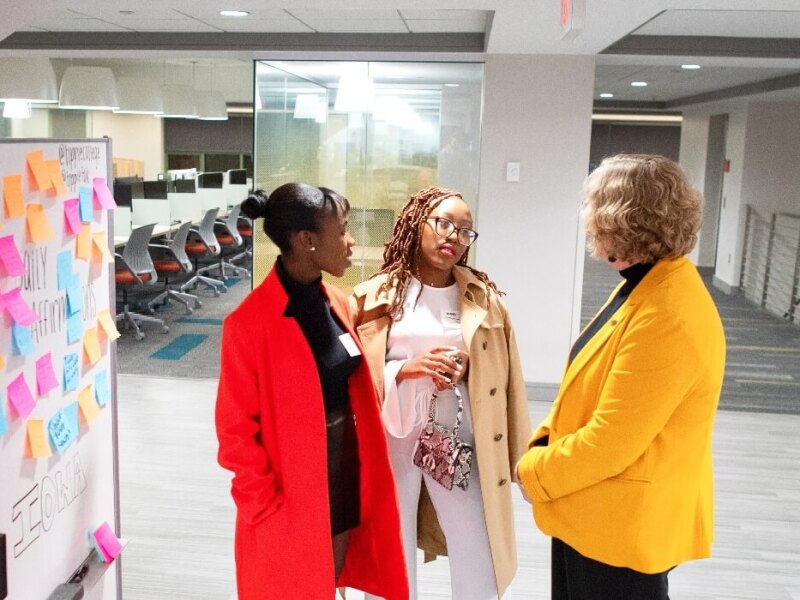Three women in jackets talking in front of whiteboard