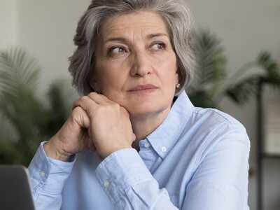 Thoughtful serious mature grey haired business lady sitting at work office table with laptop
