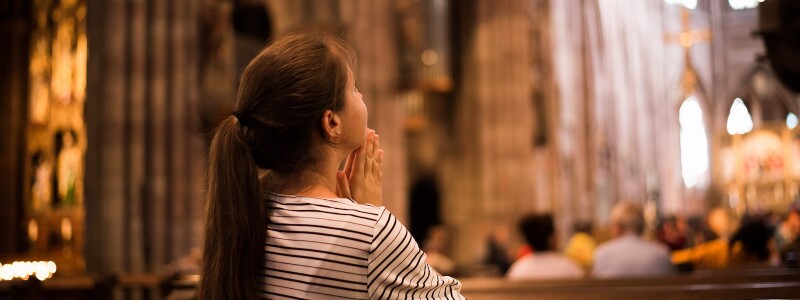 Young woman with a long pony-tail praying in a cathedral