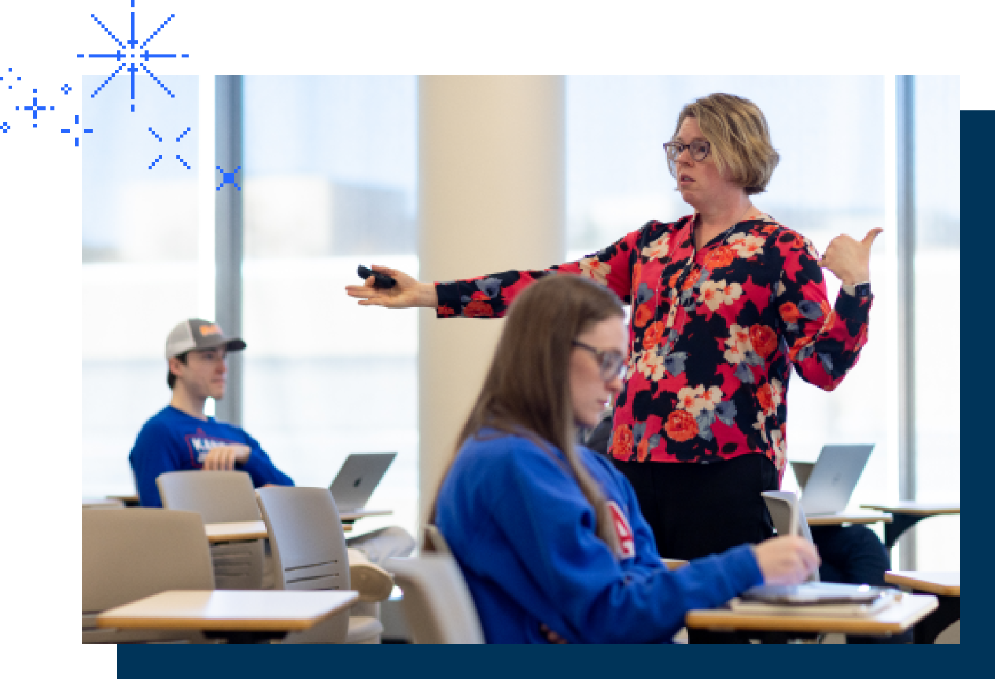 A female KU professor is standing in the middle of the classroom.