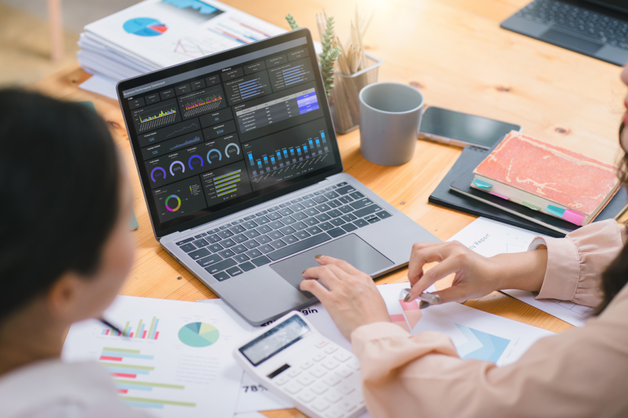 Two women seated at table with laptop analyzing charts and graphs