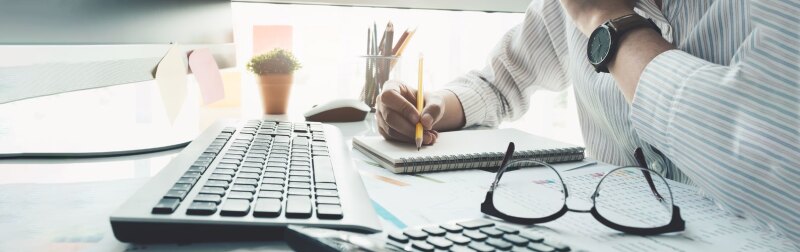 Financial analyst reviews financial report while taking notes on notepad.