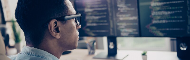 Rear view of a man worker on a computer with multiple monitors