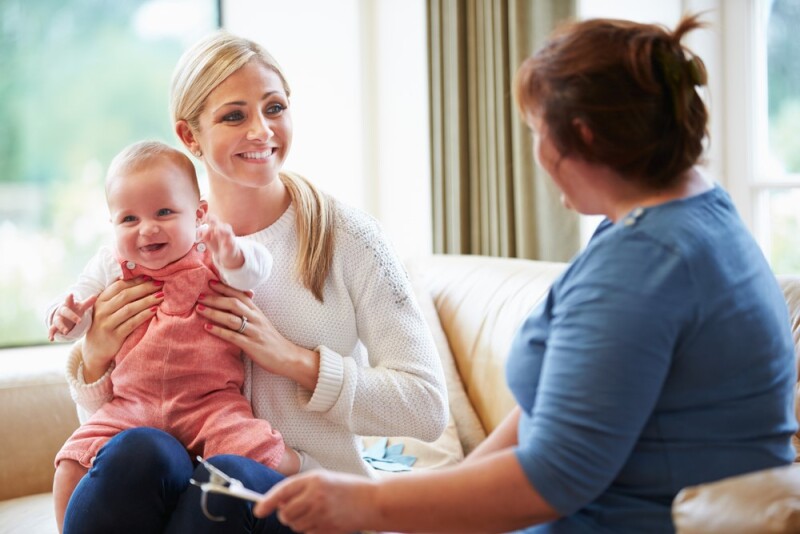 smiling woman holding baby talking to social worker