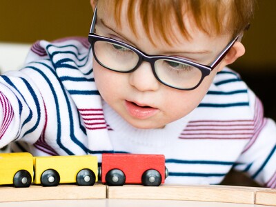 Little boy in the glasses playing with wooden trains