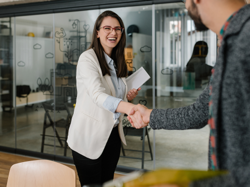 Smiling woman shaking an associates hand, with a smile on her face.