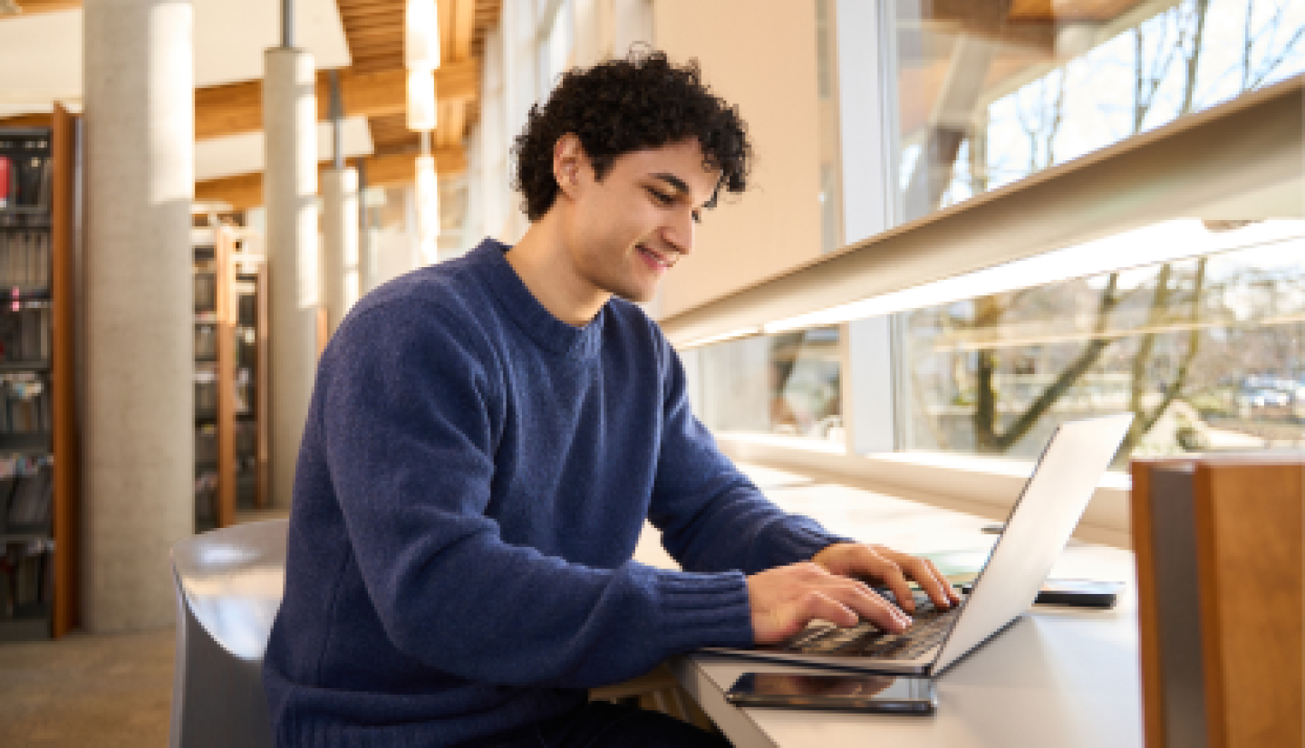 A male CWRU student sitting in campus library while working on laptop.