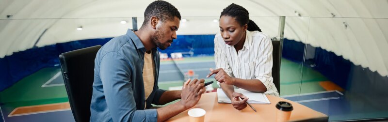 Portrait of African American sportsman reviewing practice footage with coach in training center.