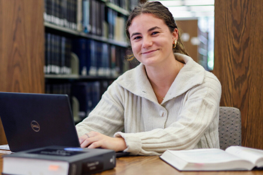 A smiling female Hofstra student working on laptop in campus library.
