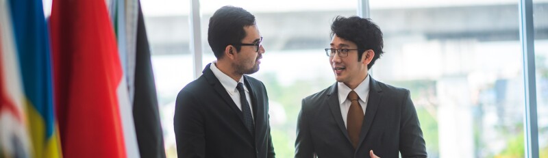 two guys standing with flags next to them appearing to be from different cultures having a conversation
