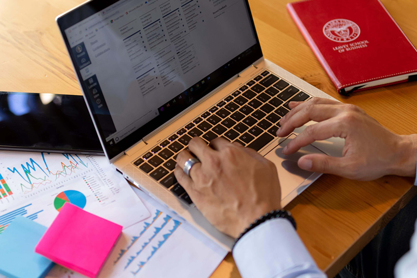 Hands typing on laptop next to notebook with Leavey School of Business logo