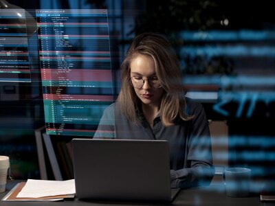 woman sitting at desk in front of laptop displaying security interface
