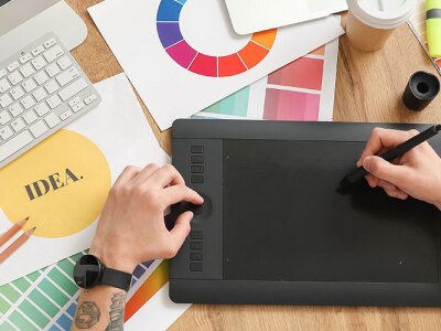 A designer working at a desk, using a drawing tablet and surrounded by various design tools and color swatches.