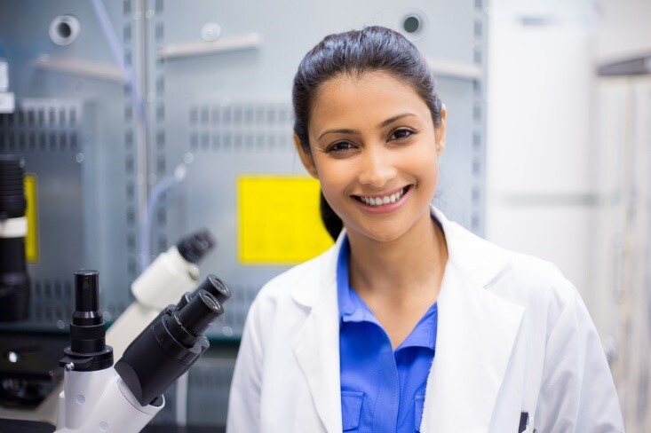woman looking straight ahead smiling next to a microscope