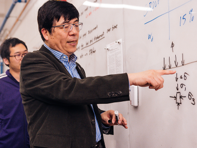 Male business professor showing equation on whiteboard to surrounding students.