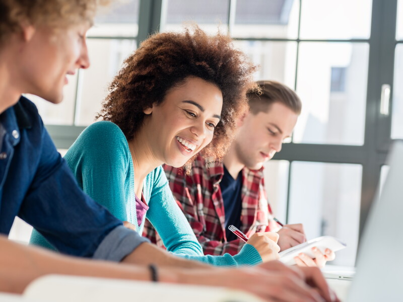 Cheerful woman writing an assignment while sitting between two classmates