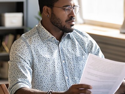 Serious-looking professional using laptop, holding document and pen