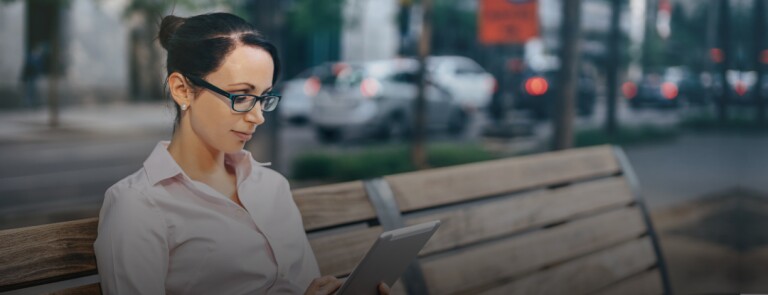 a person reads a tablet while sitting on a park bench in New York City
