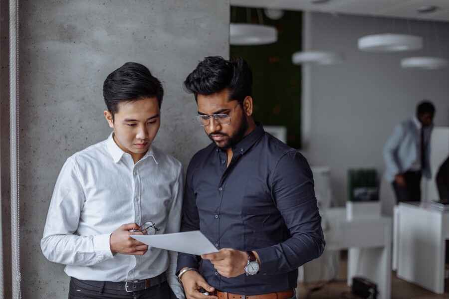 Mix raced male business partners analyzing reports against grey wall