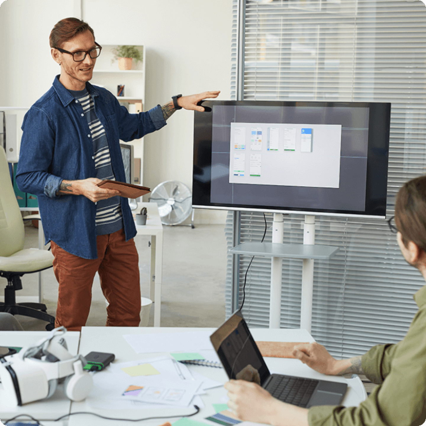 Man and woman collaborating in meeting room using large monitor and laptop