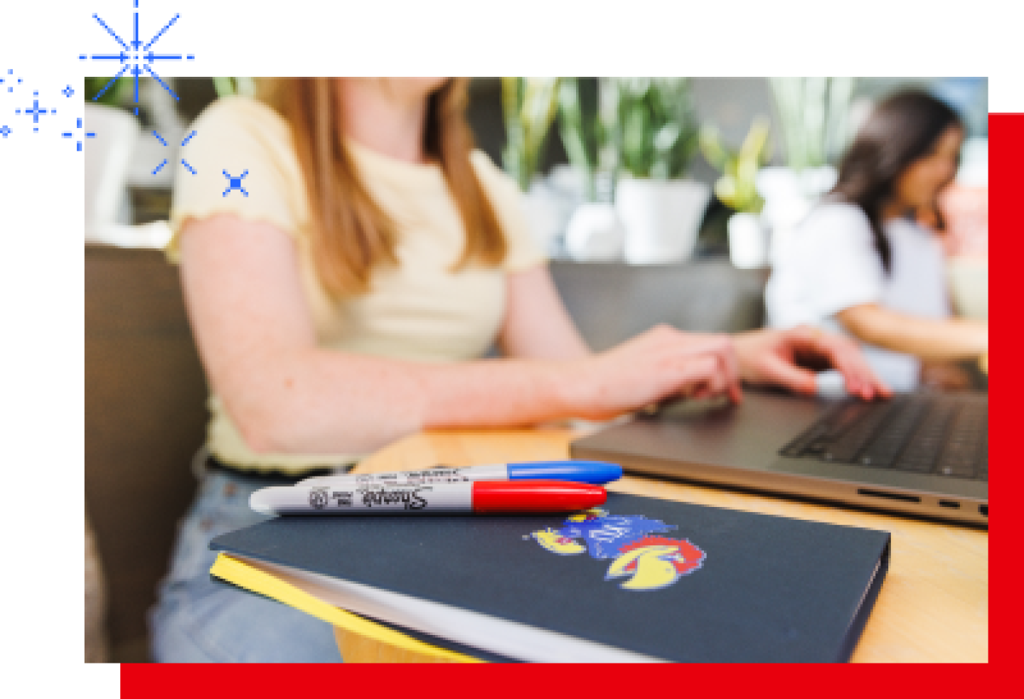A close-up of a female KU student working on a laptop with a KU journal sitting on the desk.