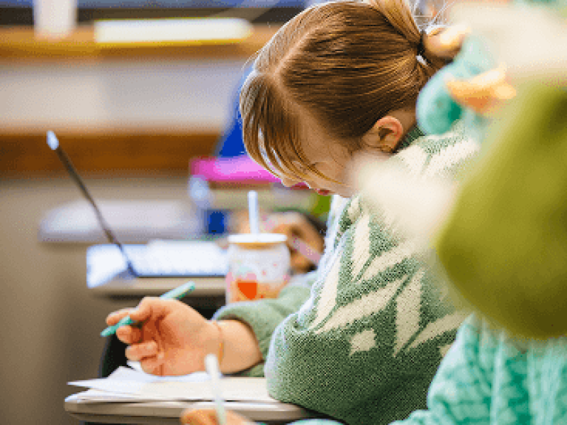Woman in green and white sweater writing at school desk