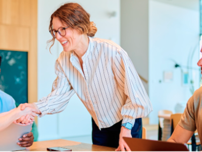 Woman in an open office setting shaking hands with someone at a table
