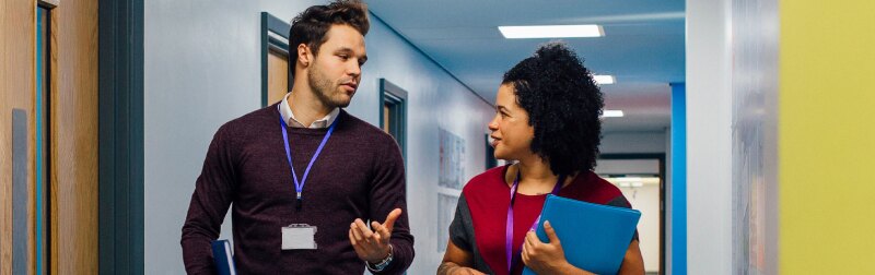 Two teachers are walking down a school hallway discussing teaching plans.