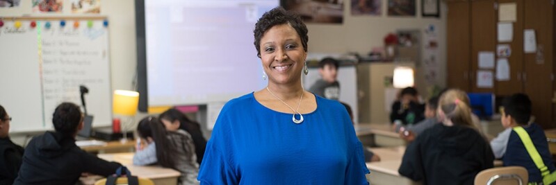 Woman standing and smiling while her class works behind her in classroom