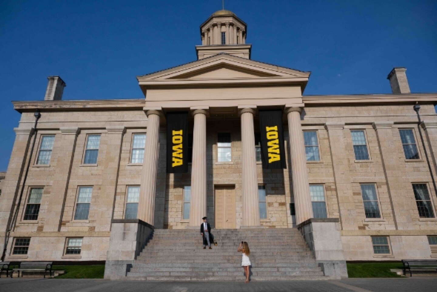Woman photographing graduate in front of Iowa campus building