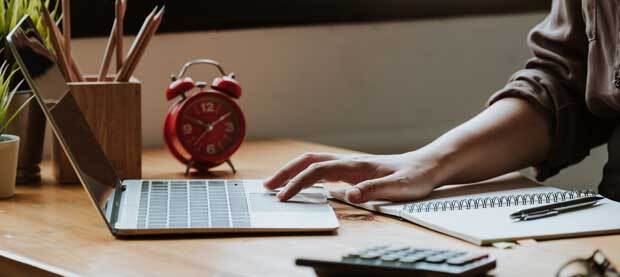 A seated student works on a laptop and a spiral notebook simultaneously