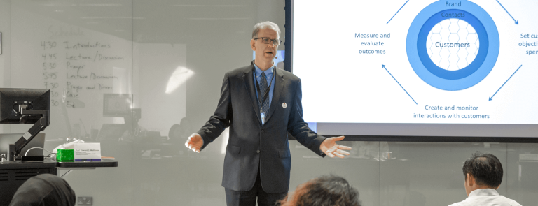 Man in suit delivering lecture to class in front of projector screen