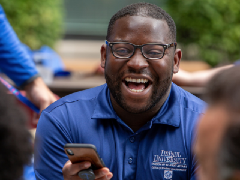 Man with glasses wearing DePaul University polo shirt and laughing